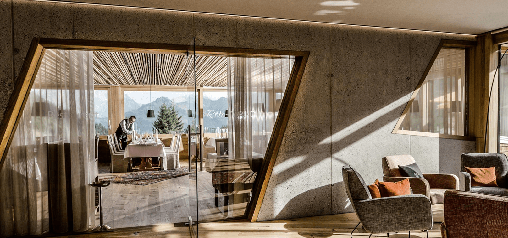 Lounge mit Glaswand und Blick in den Speisebereich mit Bergpanorama